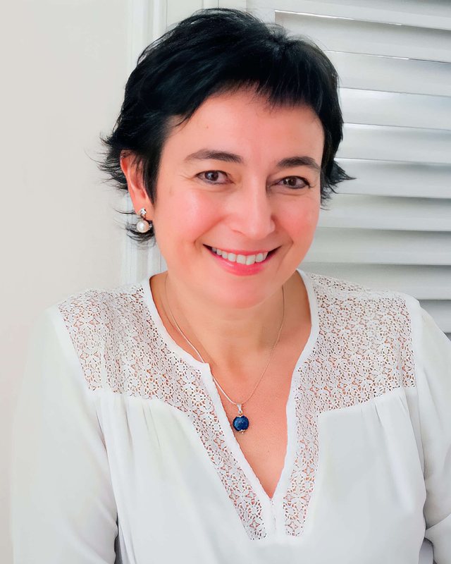 Retrato de la Dra. Natalia Caycedo, sonriente, con blusa blanca.